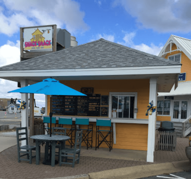 A brightly colored outdoor snack bar, featuring tables and chairs, is situated on a paved area.